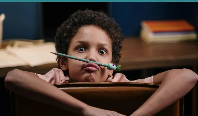 Child goofing off at a desk, balancing a pencil on their nose