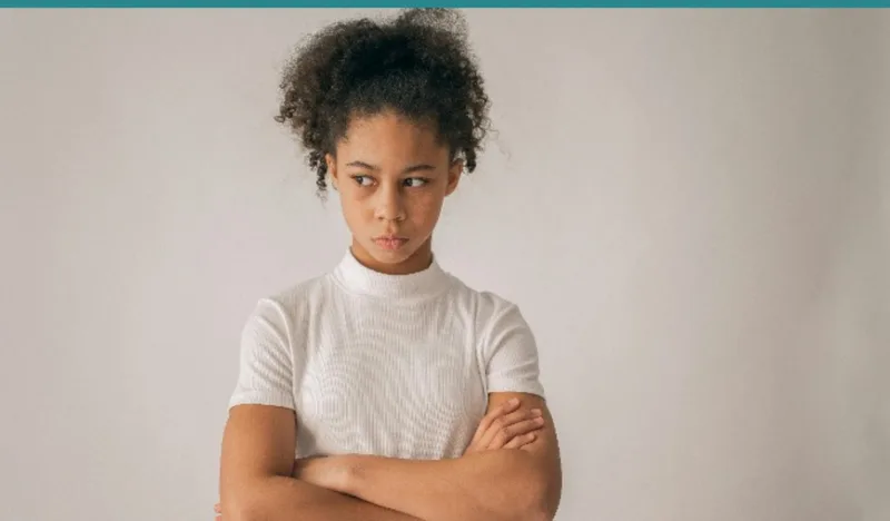 Upset child sitting outside school office waiting with arms crossed
