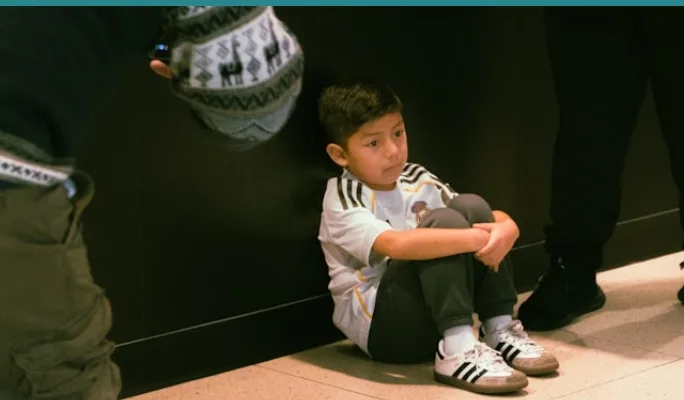 Child sitting alone against a wall at a crowded gathering