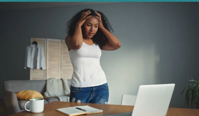 Woman with hands on head standing at a desk looking stressed