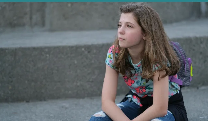 Girl with backpack sitting on steps, looking uncertain