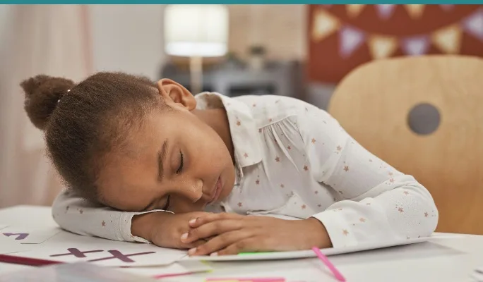Child exhausted with head down on a desk after school